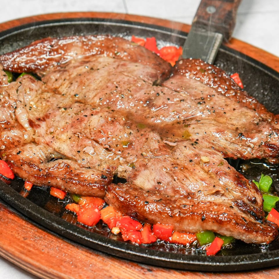 Sizzling Colombian steak with red and green peppers on a hot cast iron platter.