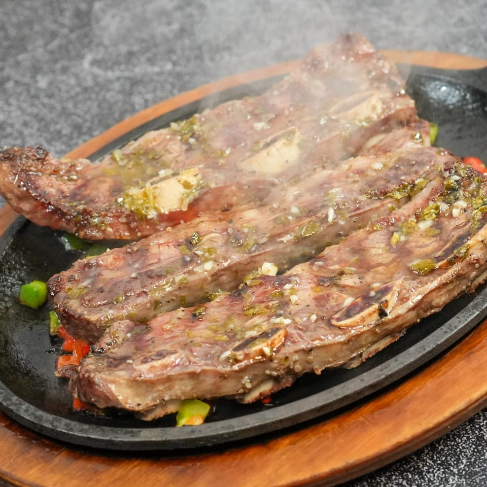 Sizzling Colombian steakhouse short ribs with green and red peppers on a hot cast iron plate.