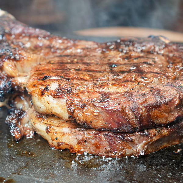 Close-up of a sizzling, perfectly seared steak with grill marks and smoke rising.
