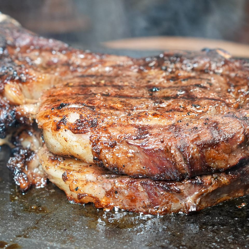 Close-up of a sizzling, perfectly seared steak with grill marks and smoke rising.