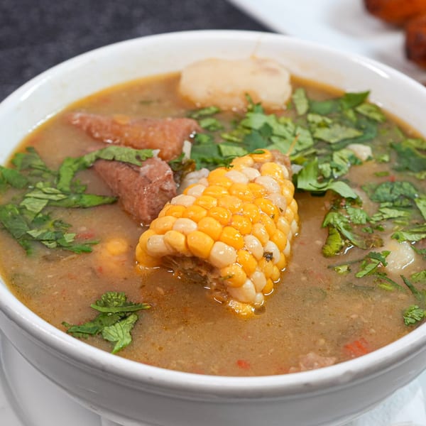 Hearty Colombian steakhouse soup with corn on the cob, meat, and cilantro in a white bowl.