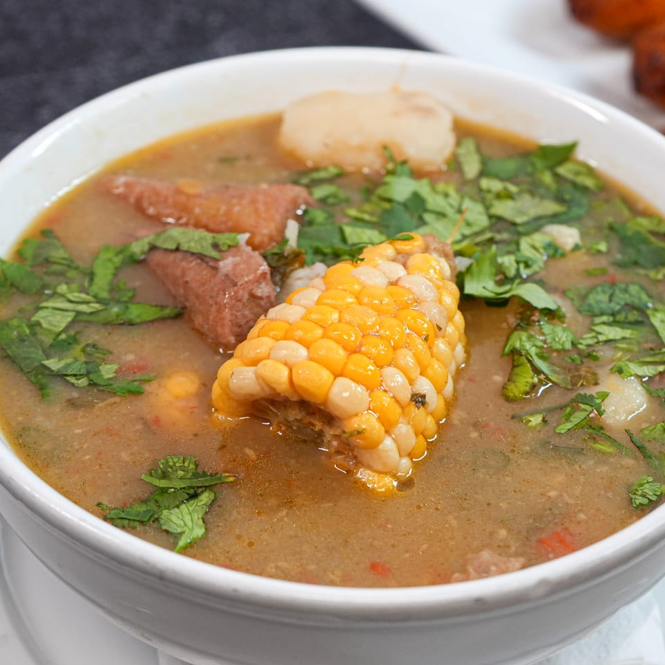 Hearty Colombian steakhouse soup with corn on the cob, meat, and cilantro in a white bowl.