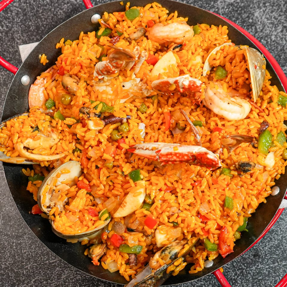A large pan of vibrant orange paella with shrimp, crab, mussels, clams, and vegetables.